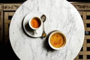 Creme brulee dessert and a cup of espresso with a beautiful old spoon on a marble table, top view